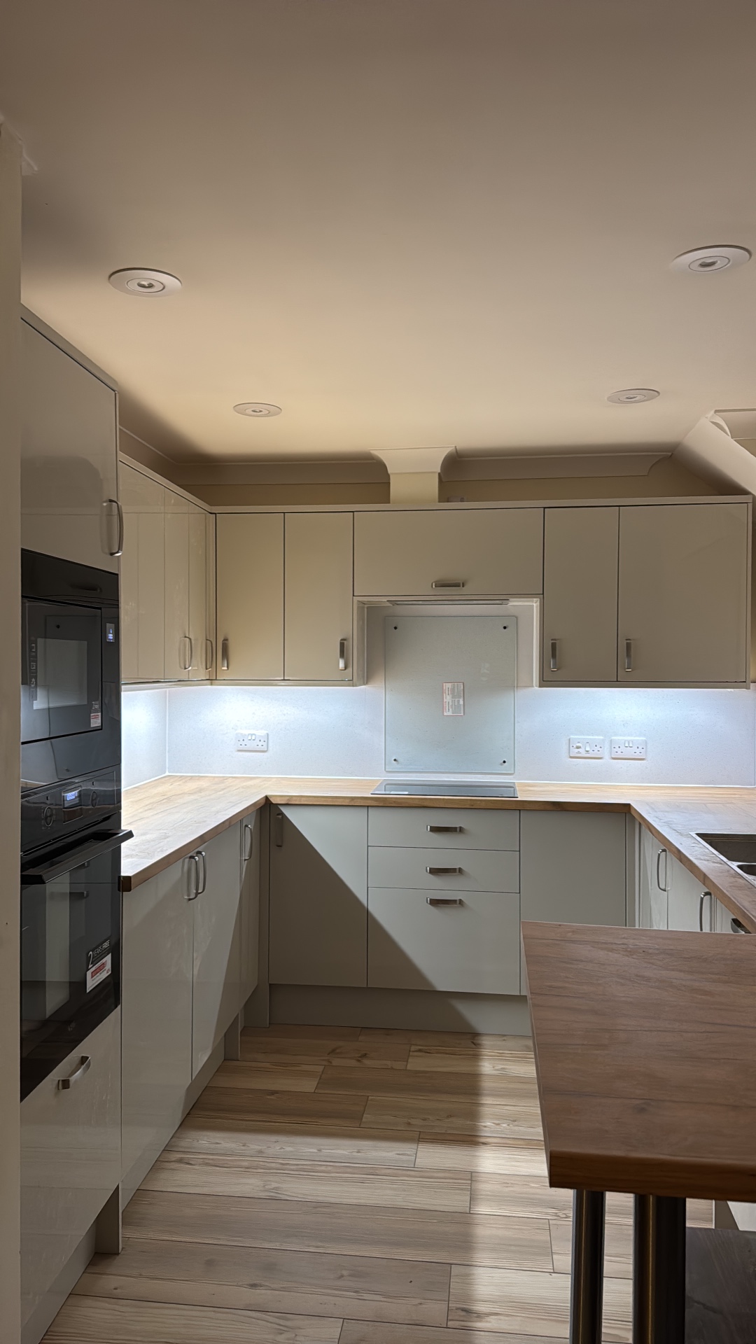 Wide view of the completed Mumbles Reno kitchen with gloss cabinets, timber worktops and under-cabinet lighting